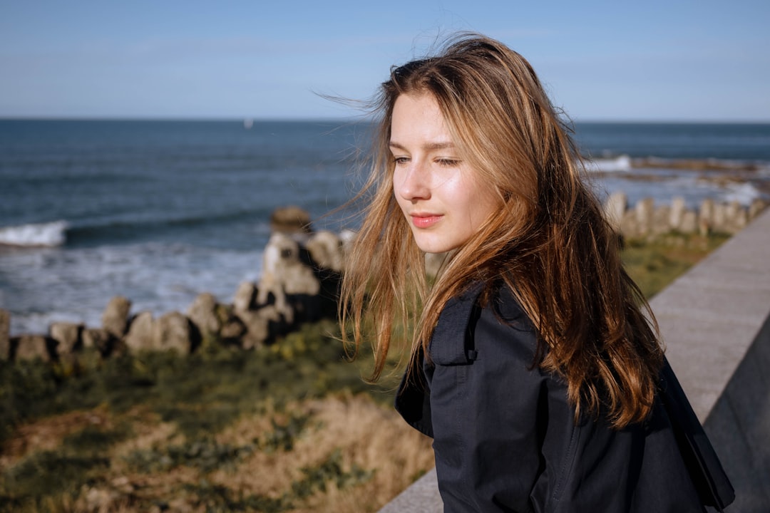 A girl stands near the sea and cliffs.