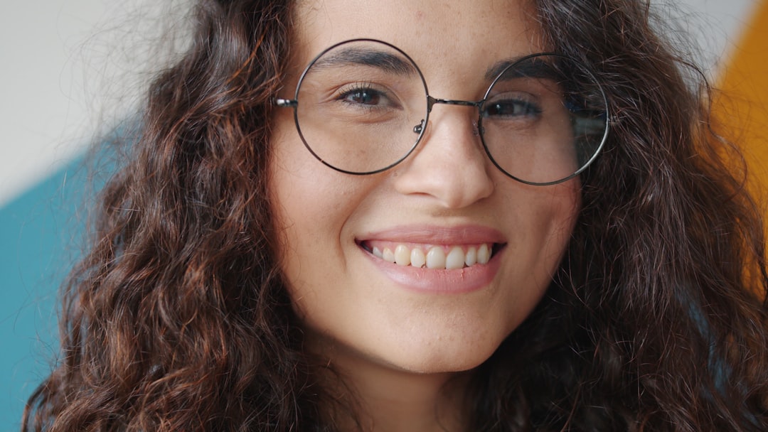 Close-up of joyful mixed race lady wearing eyeglasses smiling looking at camera indoors on colorful background, pretty girl is expressing positive emotions.