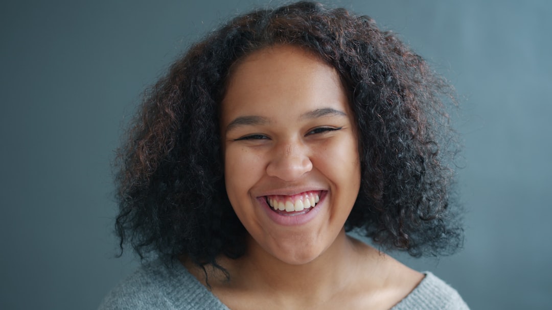Close-up of cute Afro-American lady laughing standing on gray background alone looking at camera with joyful face. Happy millennials and emotions concept.
